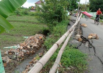Warga tetap berhati-hati saat melintasi jalan yang longsor ini. (Foto: Rochim/Tugu Jatim)