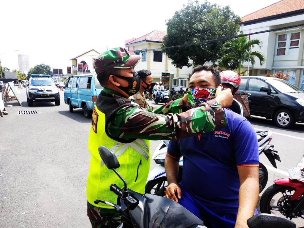 Babinsa Rembang Pasuruan terus mengimbau masyarakat agar mematuhi prokes. Warga yang tak memakai masker diberi secara gratis ketika operasi gabungan dilakukan. (Foto: Dok/Tugu Jatim)