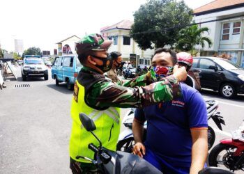 Babinsa Rembang Pasuruan terus mengimbau masyarakat agar mematuhi prokes. Warga yang tak memakai masker diberi secara gratis ketika operasi gabungan dilakukan. (Foto: Dok/Tugu Jatim)