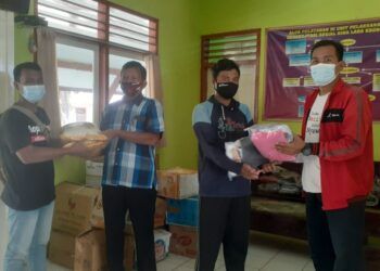 Koordinator Kegiatan Baksos Forum Biker Tuban Suwandi (berjaket merah) menyerahkan bantuan baju layak pakai dan sembako secara simbolis kepada Perwakilan UPT Rehabilitasi Eks Penderita Kusta. (Foto: Istimewa/Tugu Jatim)