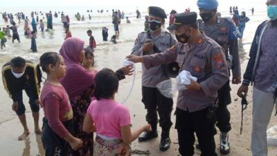 Kapolsek Palang AKP Simon Triyono tampak membagikan masker kepada warga saat melaksanakan tradisi dusdusan di pantai. (Foto: Rochim/Tugu Jatim)