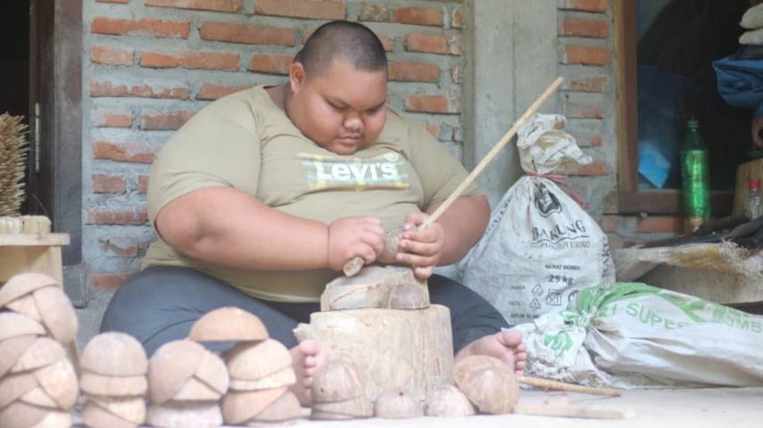 Eko Yuli Isnanto tampak konsentrasi membuat kerajinan dari cangkang kelapa untuk dijual di pasar. (Foto: Zamz/Tugu Jatim)