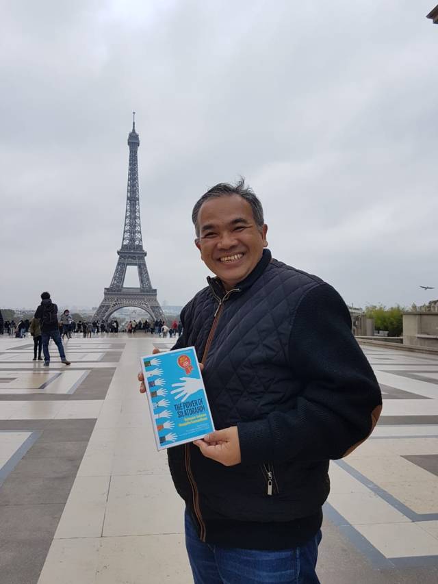 Pakar Komunikasi dan Motivator Nasional Dr Aqua Dwipayana saat berada di Paris dengan membawa buku karyanya. (Foto: Dokumen/Tugu Jatim)