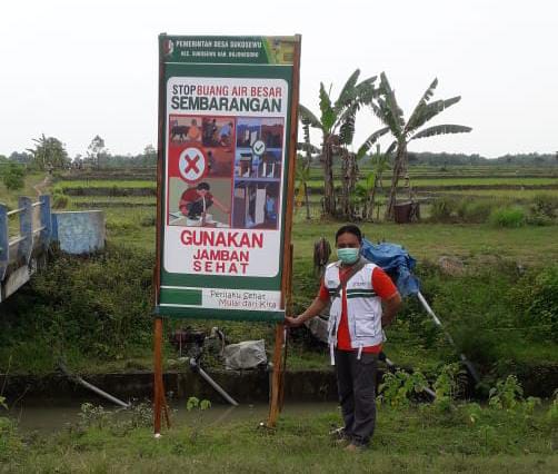 Salah satu petugas foto di spanduk yang terpasang di beberapa titik yang bertuliskan "Stop Buang Air Besar Sembarangan, Gunakan Jamban Sehat" pada Rabu (23/06/2021). (Foto: Humas Pemkab Bojonegoro/Tugu Jatim)
