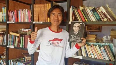 Eko Cahyono saat memaerkan salah satu bukunya di antara ribuah buku di perpustakaan miliknya. (Foto: Dokumen/Eko Cahyono)