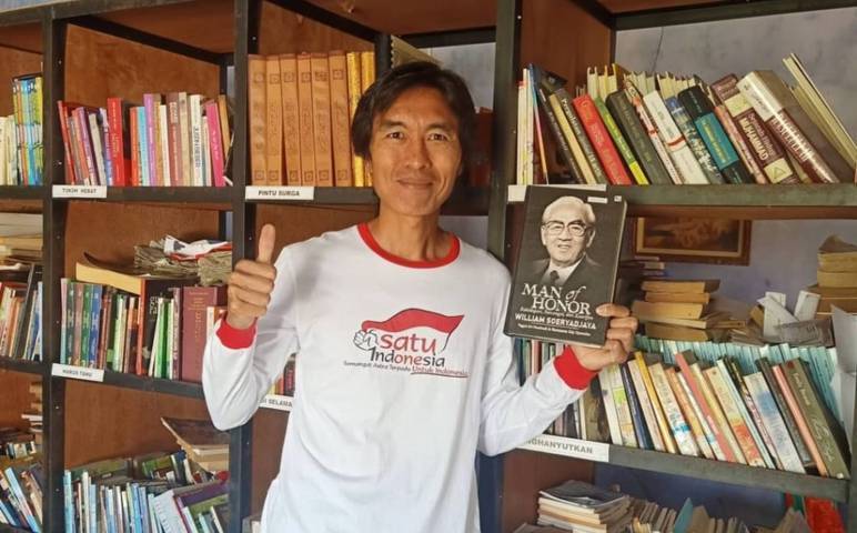 Eko Cahyono saat memaerkan salah satu bukunya di antara ribuah buku di perpustakaan miliknya. (Foto: Dokumen/Eko Cahyono)