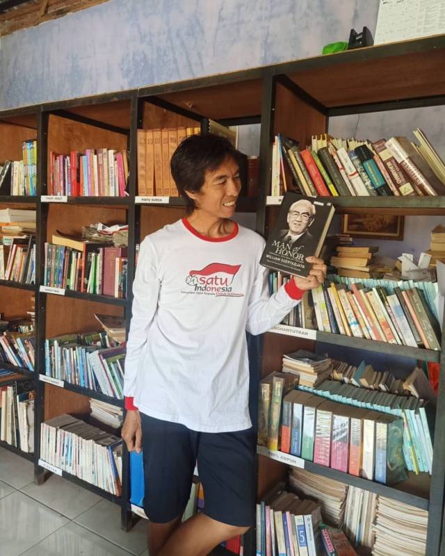 Eko Cahyono saat memaerkan salah satu bukunya di antara ribuah buku di perpustakaan miliknya. (Foto: Dokumen/Eko Cahyono)