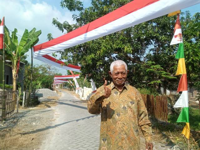 Slamet, Ketua RT Dusun Gumelem, Desa Bogangin, Kecamatan Sumberrejo, Kabupaten Bojonegoro, saat foto berlatar belakang pembentangan bendera Merah Putih sepanjang 500 meter pada Selasa (10/08/2021). (Mila Arinda/Tugu Jatim)