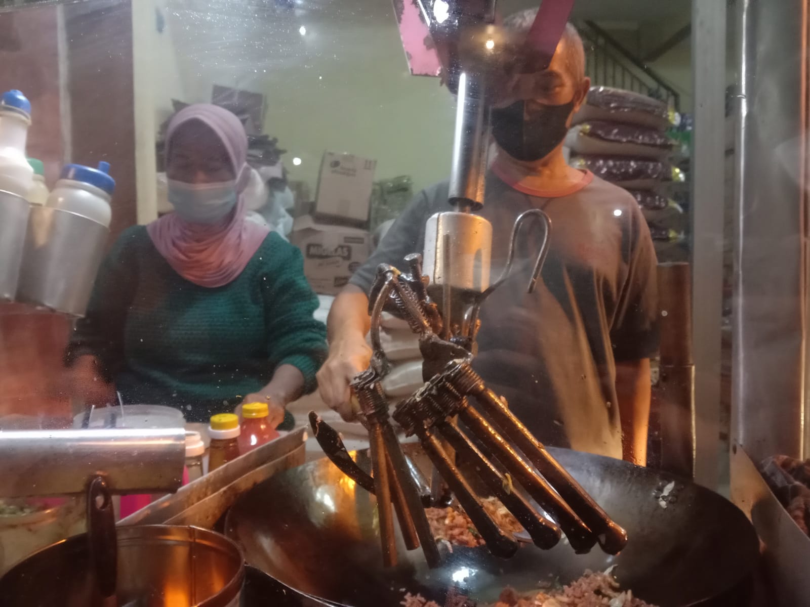 Dartadi dengan lengan kirinya yang patah memasak nasi goreng dengan mesin pengaduk hasil inovasinya serta dibantu istrinya pada Kamis malam (14/10/2021). (Foto: M. Sholeh/Tugu Malang/Tugu Jatim)