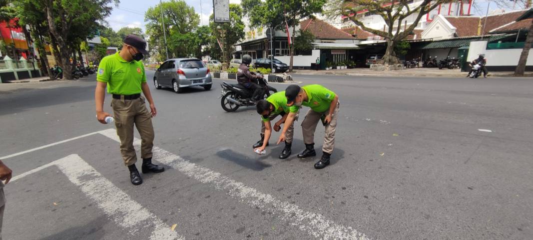 Petugas menghapus aksi vandalisme bertuliskan "Wali Kota Tewur Mundur Ji!" di jalan raya. (Foto: Istimewa/Tugu Jatim)
