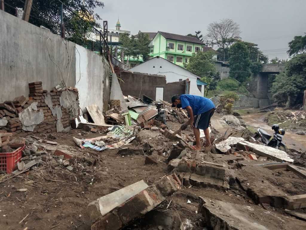Joko Joyo membersihkan puing-puing bangunan rumahnya yang roboh diterjang banjir bandang di Kota Malang pada Kamis (04/11/2021). (Foto: M. Sholeh/Tugu Malang/Tugu Jatim)