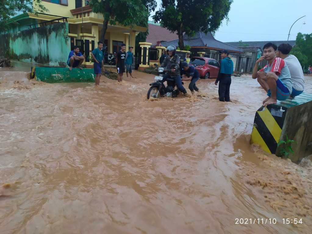 Warga membantu kendaraan yang akan melintasi jalan raya yang banjir akibat hujan deras yang mengguyur wilayah Tuban selama 3 jam pada Rabu (10/11/2021). (Foto: Dokumen/Tugu Jatim)