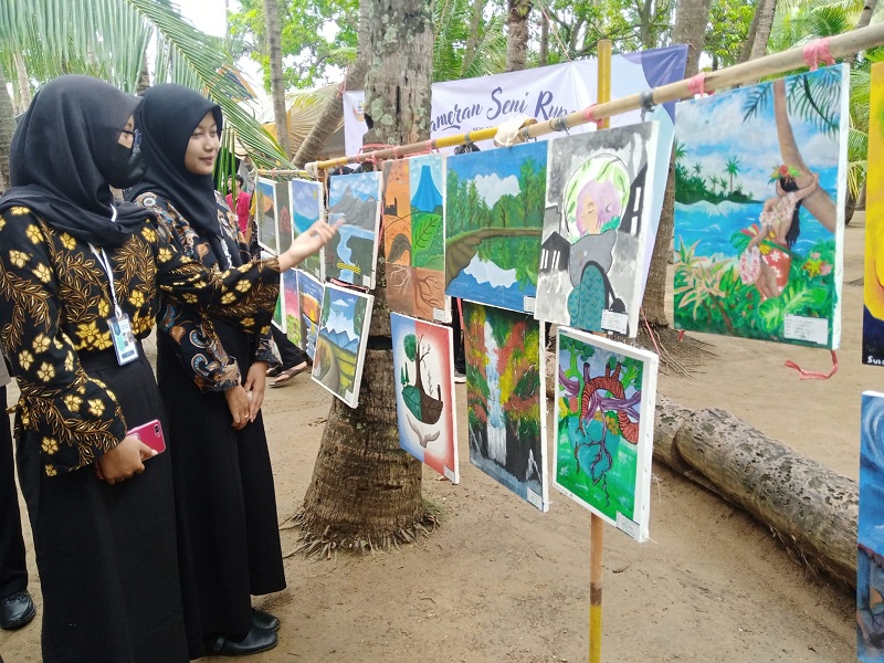 Pengunjung menikmati karya lukisan seniman pelajar di Wisata Pantai Kelapa, Tuban, Sabtu (14/5/2022).