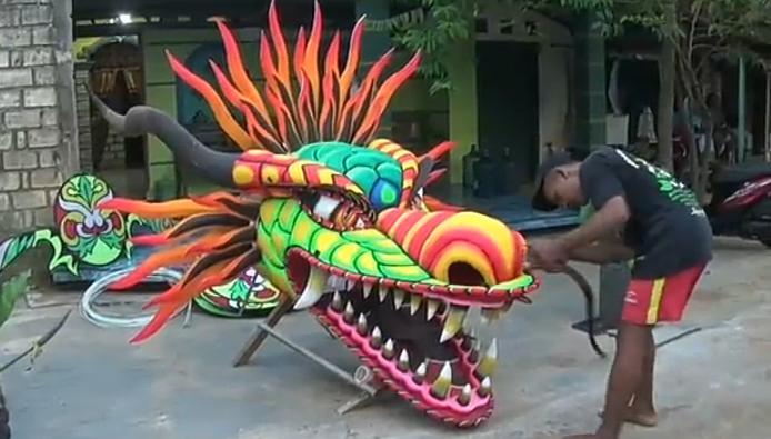 Ilham tampak sibuk merangkai dan memasang beberapa komponen layang-layang naga hasil orderan pelanggannya.