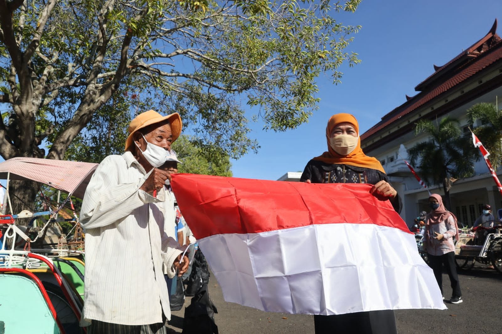 Gubernur Jawa Timur Khofifah Indar Parawansa ketika membentangkan bendera merah putih bersama dengan tukang becak.