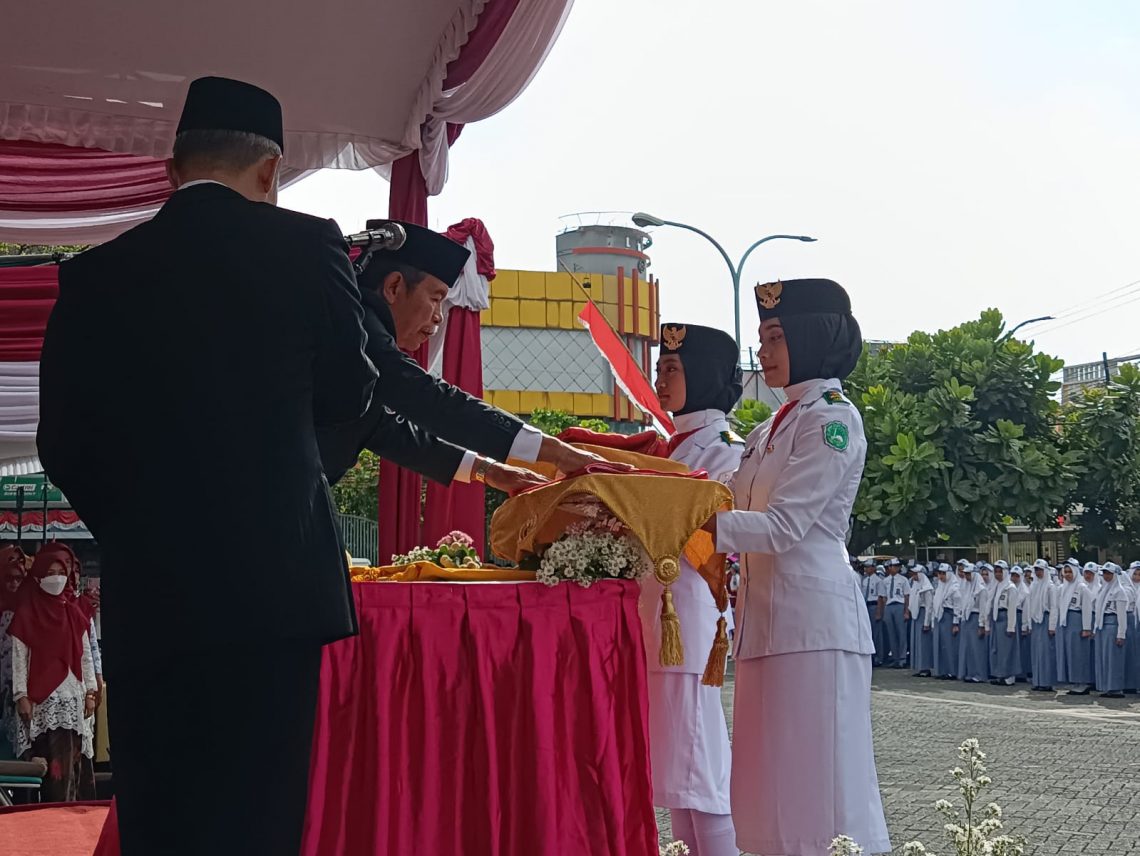 Inspektur upacara, Drs H Moh Ishom Ihsan memberikan bendera merah putih kepada petugas upacara. Foto: Yona Arianto/Tugu Jatim